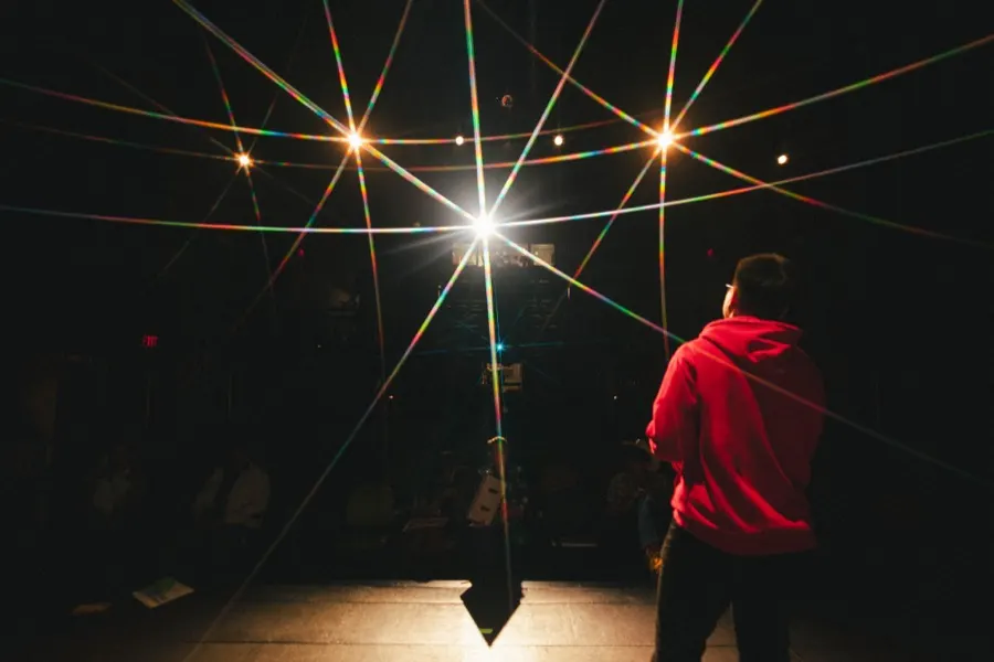 A figure on stage under a wide starburst of light.